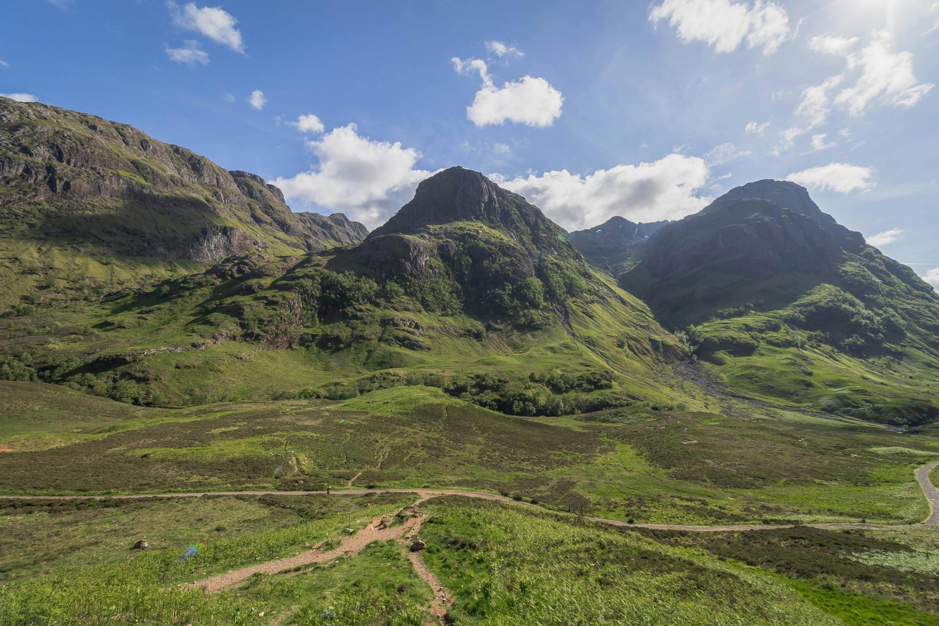 Breathtaking view of the Three Sisters in Glencoe, Scotland under a vibrant summer sky.